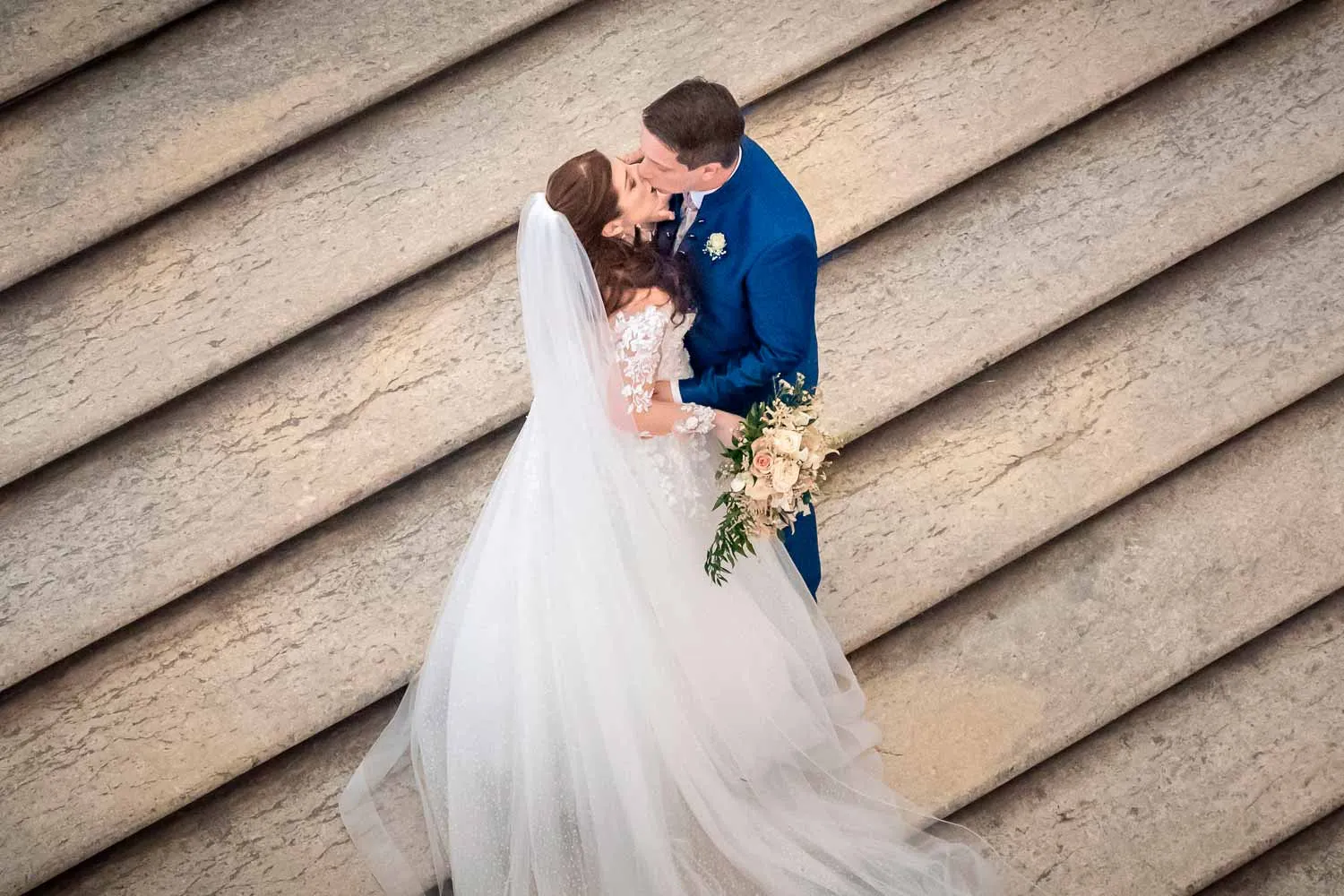 Aerial view of bride and groom kissing on a sunlit stone staircase — oemme photography